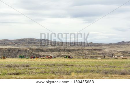 Various modern farming equipment parked in a pasture in a valley with mountains and hills in the background in Montana landscape