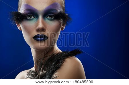 Space beauty. Horizontal portrait of a young woman wearing professional artistic makeup with feathers against blue background