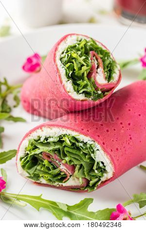 Red pancakes with sheep cheese and rucola on white plate.