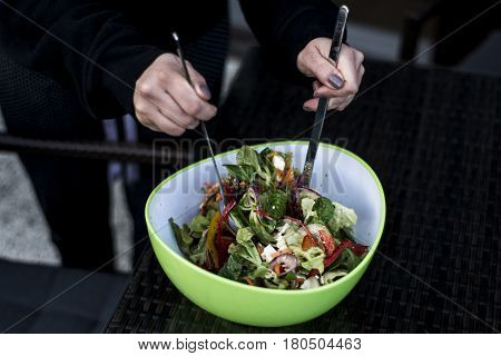 Delicious fresh and healthy salad in a green bowl mixed by a woman hands with salad spoon food