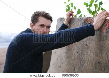 Bearded man in sweater leant on the wall.