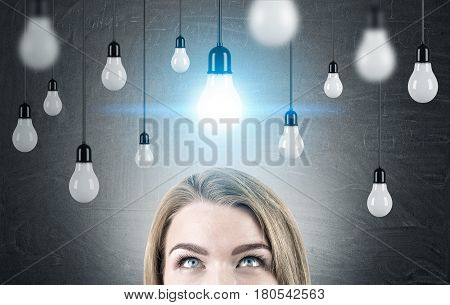 Close up of a head of a woman with blond hair standing near a blackboard with many light bulbs hanging on wires. Toned image