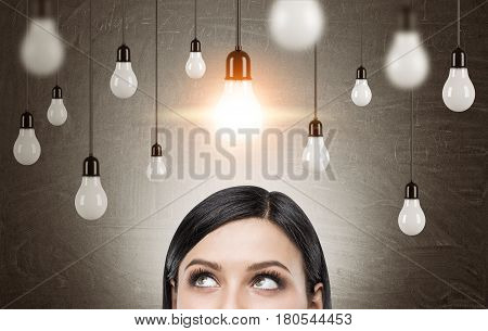 Close up of a head of a black haired woman standing near a blackboard with many light bulbs hanging on wires. Toned image