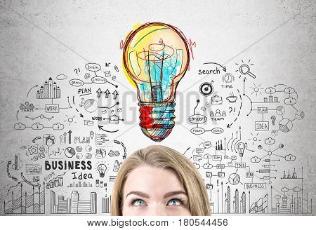 Close up of a head of a woman with blond hair standing near a concrete wall with a business idea sketch drawn on it.