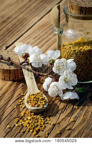 Grains of bee pollen in jar and wooden spoon on wooden table with decoration flowers. Apitherapy. Bee products