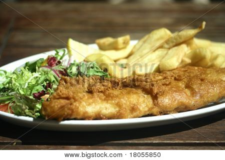 Balık ve cips ahşap bir masa tarafta yeşil salata ile bir tabak
