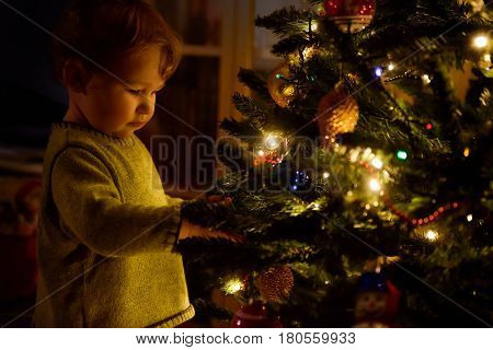 Baby looks at decoration on a Christmas tree at home. The one-year child during the Christmas and New Year holidays.