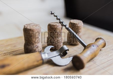 Vintage beer bottle opener and corkscrew with wooden shabby handles of pleasant light brown color lying on a wooden table. Next to them lie three wine corks. Bar stuff concept