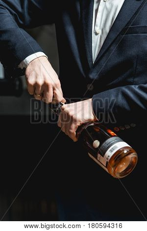 Sommelier in a dark blue jacket opens a bottle of rose wine.
