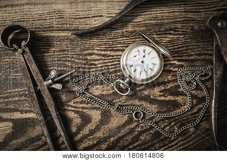 Composition with vintage pocket watch. Old rusty tools and a clock on a dark wooden background. Watch repair