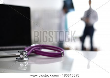 Laptop and stethoscope on the desk , doctors standing in the background.