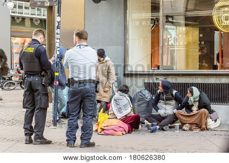 Two policemen looking at the paipers of some immigrants who are sitting on the street. Copenhagen Denmark - April 6 2017