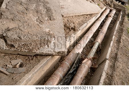 Old rusty water pipes in concrete trench. Underground utility and services pipe lay at the construction site. Repairing of water delivery system, vintage color.