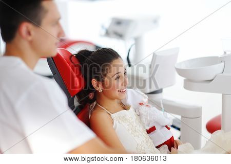 A dentist a man talking to a child patient a girl and telling her about oral hygiene