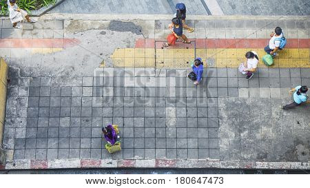 On street walk in top view man and woman with shopping bags stand on square block pedestrian walk way with yellow and red line for guide blind people walk (aerial city street view)