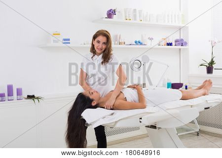 Woman beautician doctor with patient in spa wellness center. Portrait of a young female professional cosmetologist make head massage to beautiful brunette girl in cosmetology cabinet or beauty parlor.