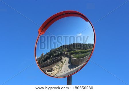 traffic mirror showing a narrow street against blue sky meditteranean scene