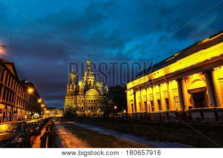 Illuminated Church on Spilled Blood with dark sky in Saint Petersburg, Russia. Griboyedov canal and busy street with many cafes, restaurants and shops