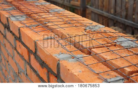 Close up on laying building bricks with iron grid to better wall strength. Building house wall. It is almost impossible to build brick walls that contain steel reinforcing bars.
