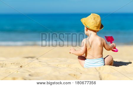 baby boy sit back with toys and sand on beach