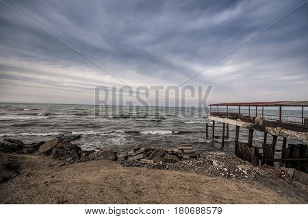 Beautiful Surreal Landscape Of Abandoned House And Ladder On Rocky Seashore At Sunset Time. Cloudy W