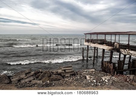 Beautiful Surreal Landscape Of Abandoned House And Ladder On Rocky Seashore At Sunset Time. Cloudy W