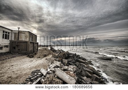 Beautiful Surreal Landscape Of Abandoned House And Ladder On Rocky Seashore At Sunset Time. Cloudy W