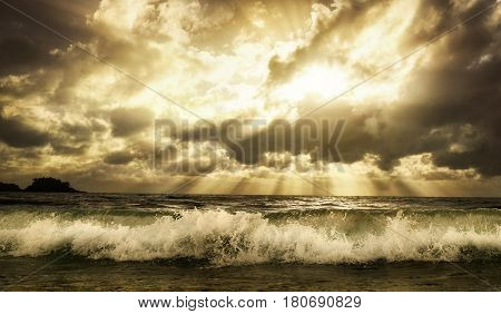 Dramatic cloudscape over the sea with rays of sunlight and a foaming wave in the foreground toned warm colors
