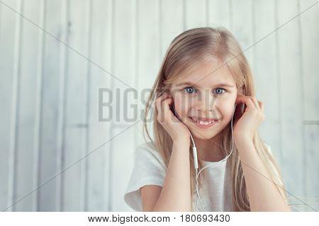 Smiling girl is listening to the music through her earphones and looking at the canera