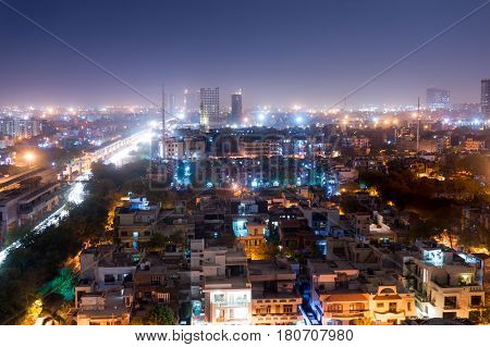 Noida cityscape at night with houses, office, skyscrapers, streets and metro rails visible. Lots of construction is visible as well showing the development