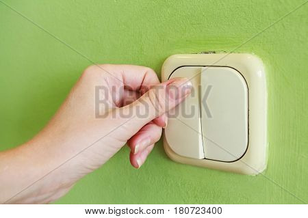 Female hand pressing two keys beige light switch mounted on green wall