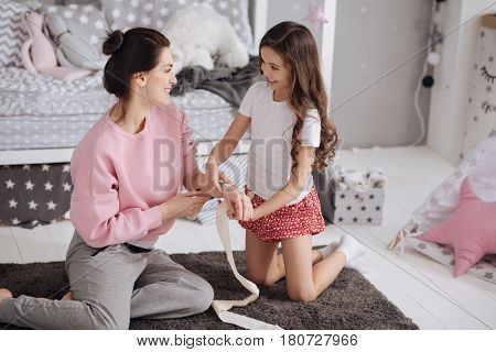 Enjoying medicine lesson with my mother. Lively little gifted girl sitting in the night nursery and caring about mother while using elastic roller and bandaging