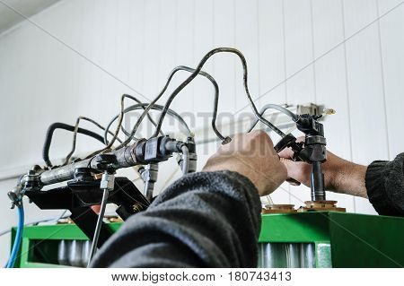 Mechanics a repairing a diesel injector. Worker's hands installs injector on a Test Bench Machine. A man checks a work of a nozzle.