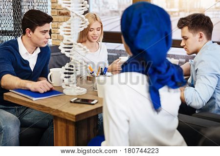 Work in group of four. Cheerful diligent international students sitting at the table and working on the project work in genetics