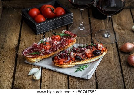 Wine appetizer set. Glass of red wine, brushettas with fresh tomato and jamon on over rustic grunge wooden background