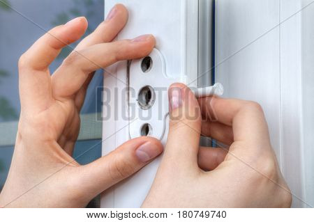 Close-up of the hand of a locksmith installing a window limiter on a plastic frame.