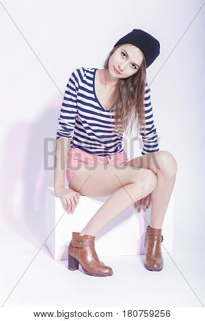 Fashion Youth Lifestyle Concepts. Portrait of Cute Smiling Caucasian Slim Brunette in Hat and Striped Shirt Posing in Studio Against White. Wearing High Heels.Vertical Image