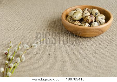 Wooden plate with quail eggs and with twigs of willow on a linen tablecloth. Selective focus. Copy-space composition