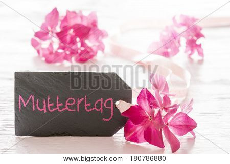 Plate Of Slate With German Text Muttertag Means Mothers Day. Spring Flower Blossom Of Hydrangea. Shiny White Wooden Background