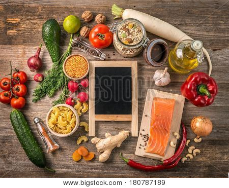 Various veggetables, spices, pasta and rustic bottle of oil, black chalkboard in center, topview