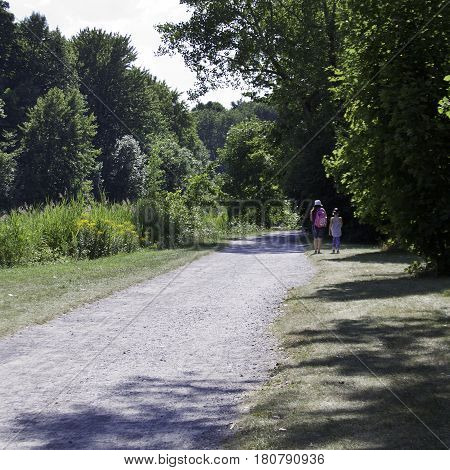 Lasalle, Quebec, August 2, 2016 - Square view from the back of a woman and child walking along a path among the trees and foliage in Angringnon Park, Lasalle, Quebec on a sunny day at the beginning of August.