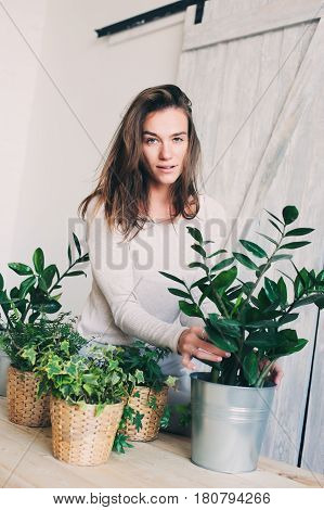 young woman watering flowerpots at home. Casual lifestyle series in modern scandinavian interior