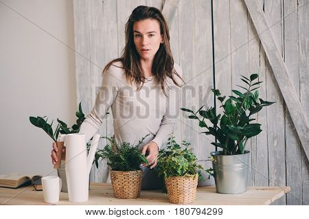 young woman watering flowerpots at home. Casual lifestyle series in modern scandinavian interior