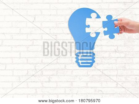 Digital composite of Hand with jigsaw light bulb on brick white wall