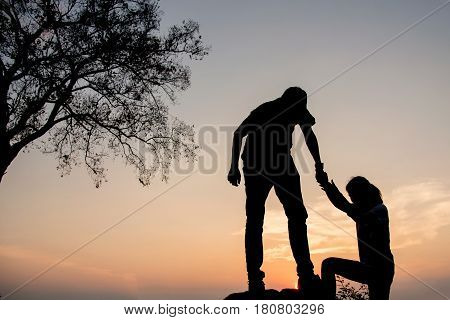 People helping each other hike up a mountain at sunrise. Giving a helping hand and active fit lifestyle concept.