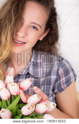 A girl with braces posing against a brick wall background with a bouquet of tulips. Dental concept
