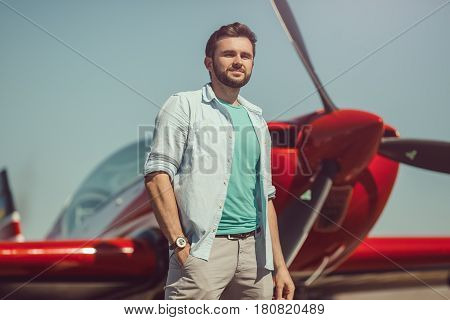 Pilot and airplane. Cheerful handsome young man pilot standing near small sport plane