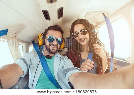 Happy smiling couple making selfie with smartphone inside plane cabin during flight. Young man and woman enjoying trip