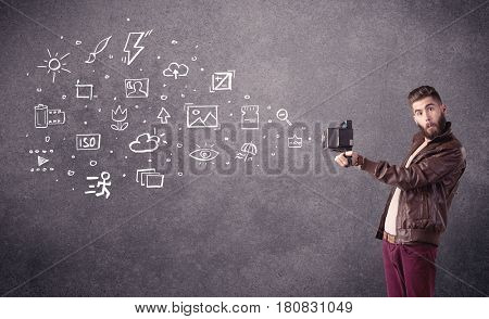 An elegant hipster guy trying to use a vintage camera with camera settings icons drawn on wall, like flash, white balace or ISO value concept