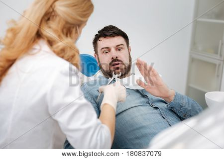 No way. Handsome expressive young man looking scared and unwilling having his teeth out while paying a visit to his doctor